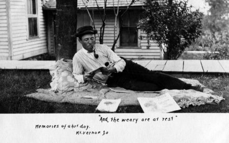 photo of Unidentified Man Lying Down While Reading and Smoking a Pipe