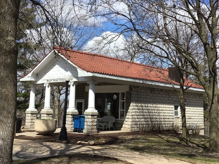 Example of a Greek Revival building.  1-story stone building with large porch with roof held by 4 large white round pillars.