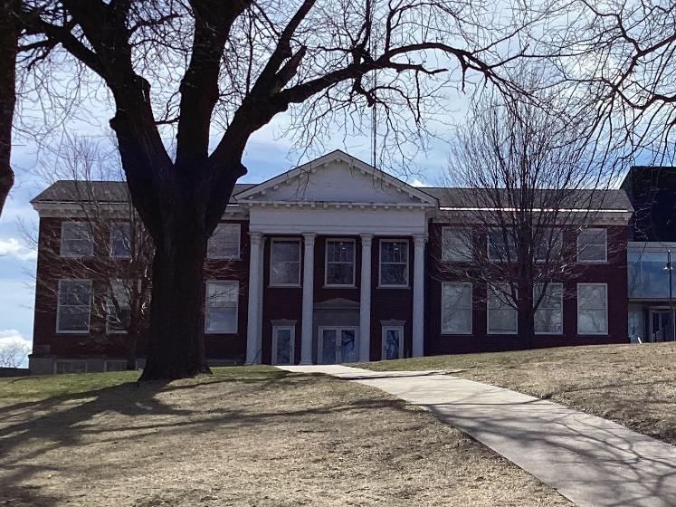 2-story red brick college building with large white round pillars holding up a porch roof.  Example of a Greek Revival style.