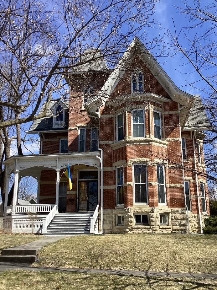 3-story red brick home with tall thin windows and high peaked roof.  Example of Gothic Revival style.