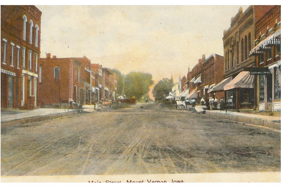 Postcard featuring Mount Vernon’s Main Street.  The card shows a view from the center of Main St. as a dirt road and wooden sidewalks line the brick buildings on each side.