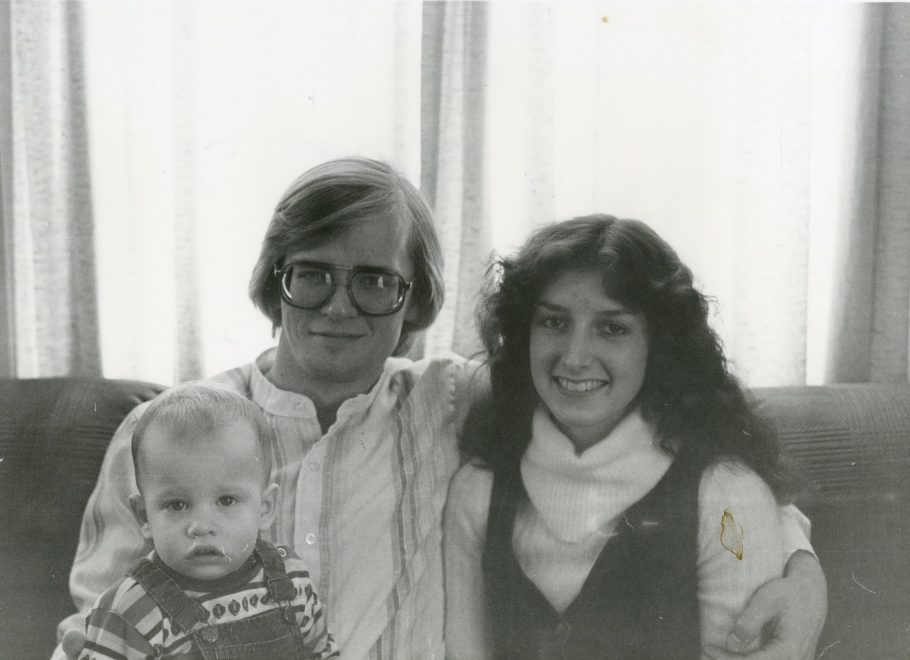 Photo of Glenn, Kim and son Zachary Wolfe sitting on a couch in front of large windows.