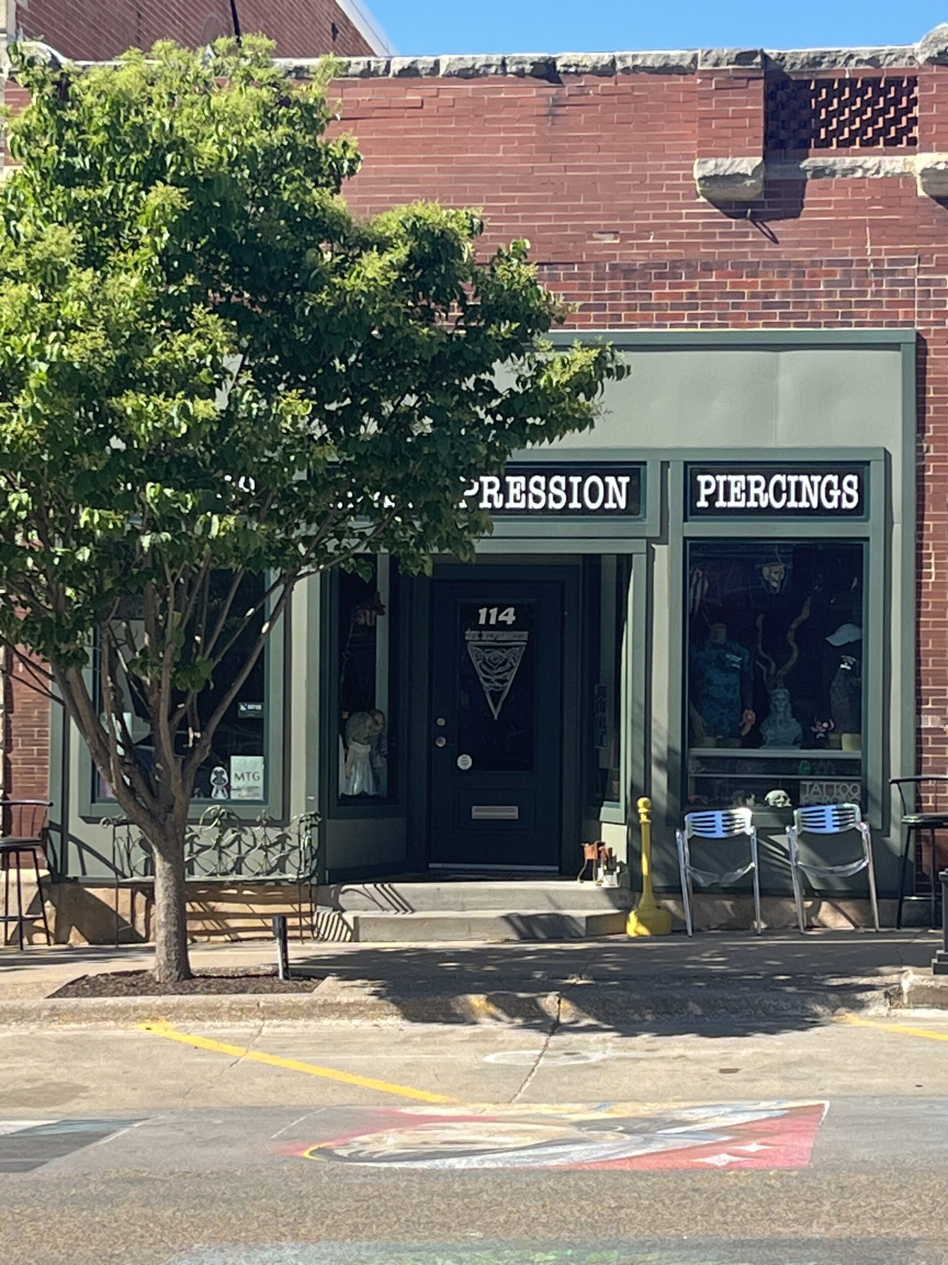 Ink Expression Tattoo and Piercing is a red brick building with green framing around the windows and door.