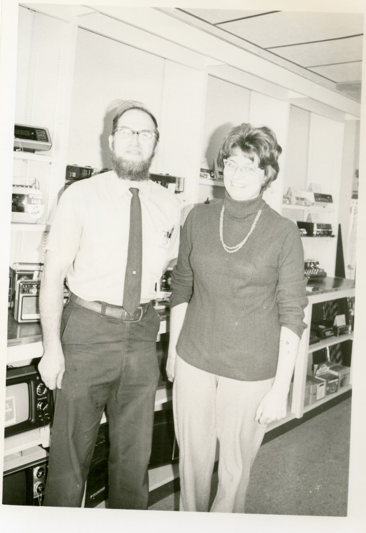 Black and white photo of Dean and Pat Traver standing in front of some small kitchen appliances that they are selling.