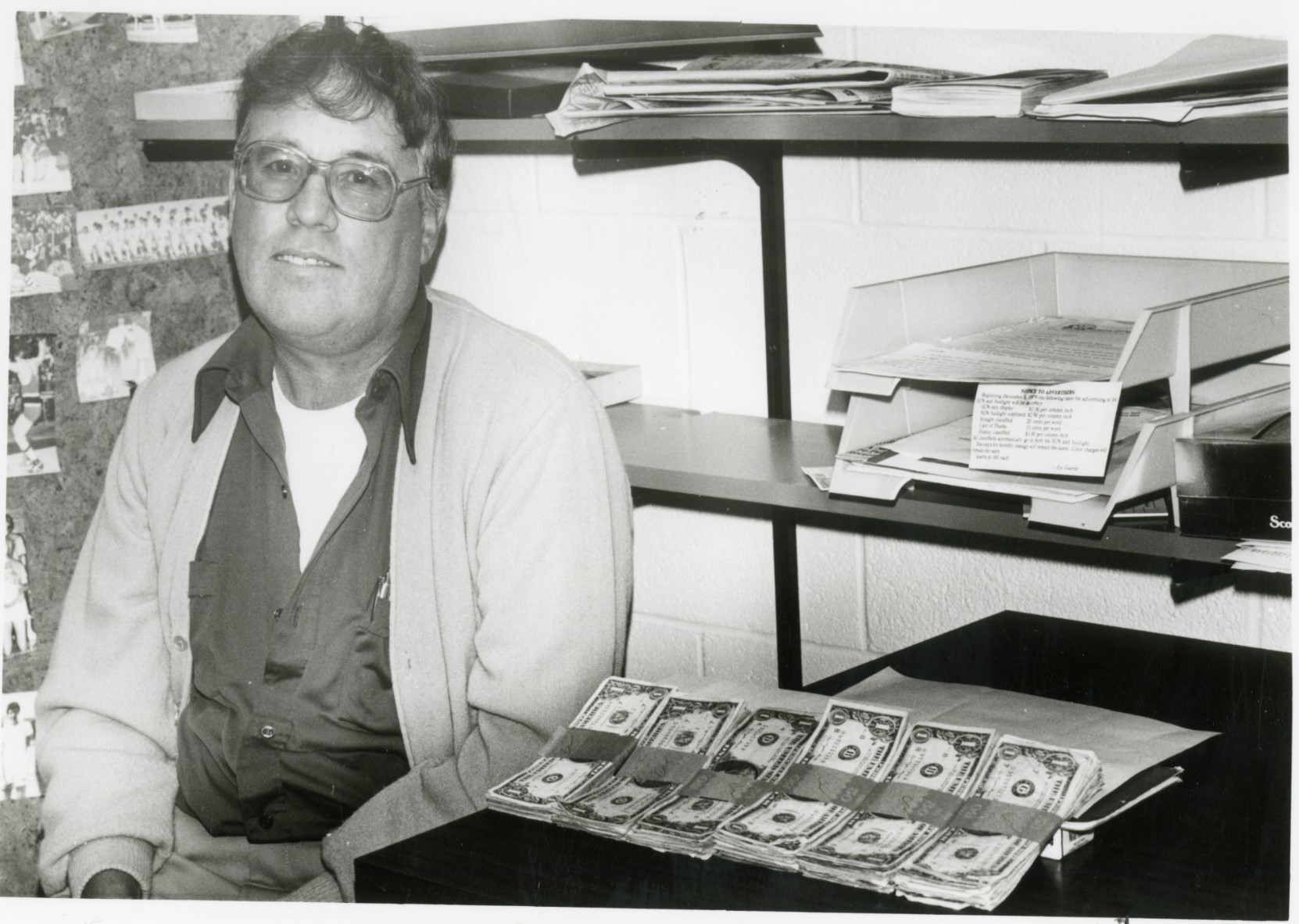 Black and white photo of Bob Wolfe sitting next to piles of cash.