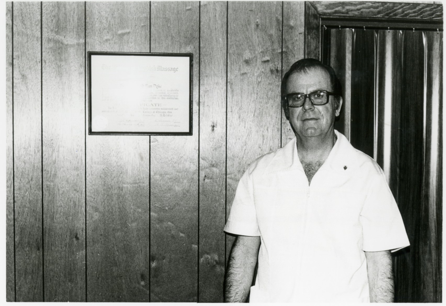 Black and white photo of Henry Van Dyke standing in front of his Swedish Massage Certificate.