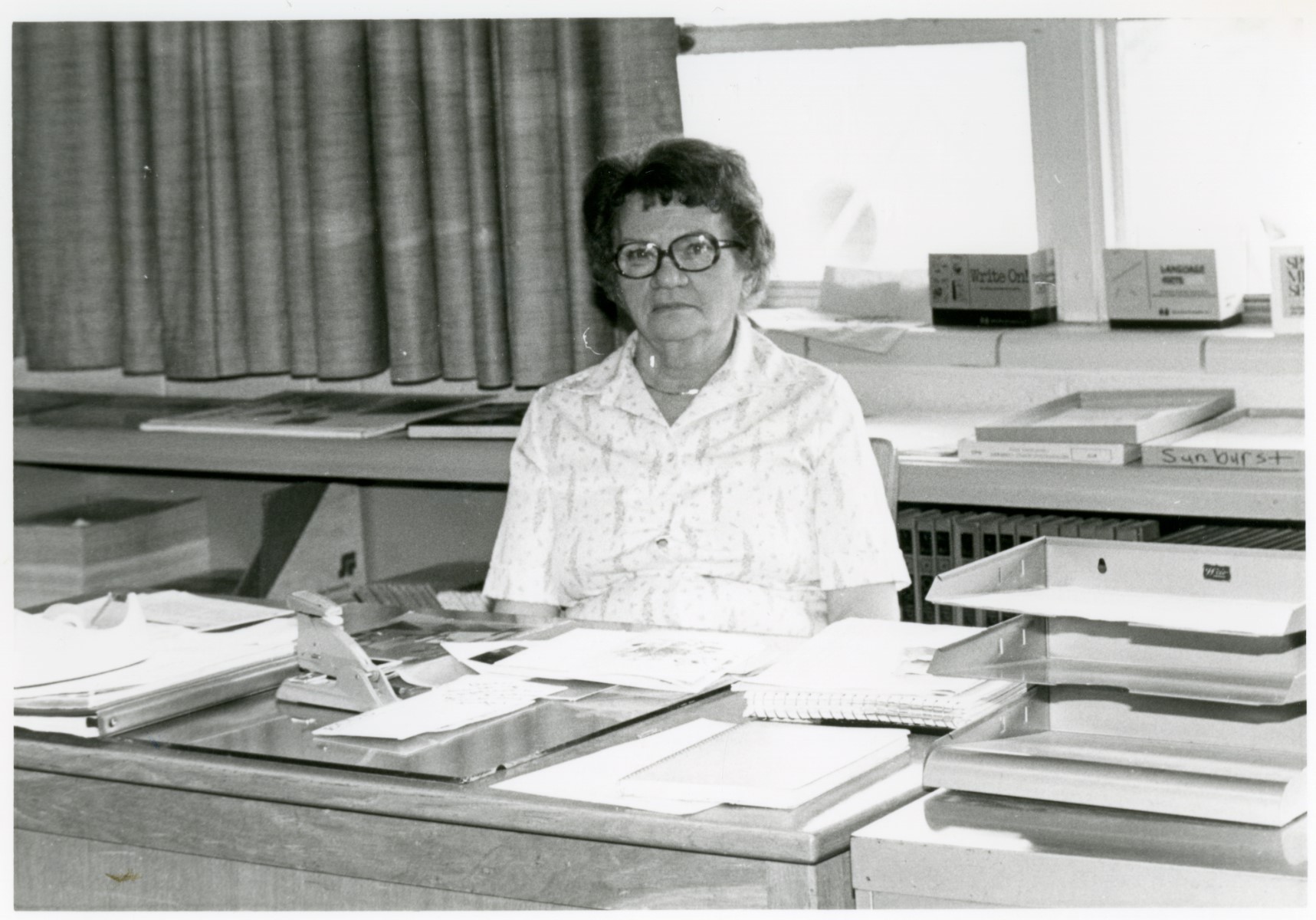 Black and white photo of Verla Scheetz standing behind a desk.