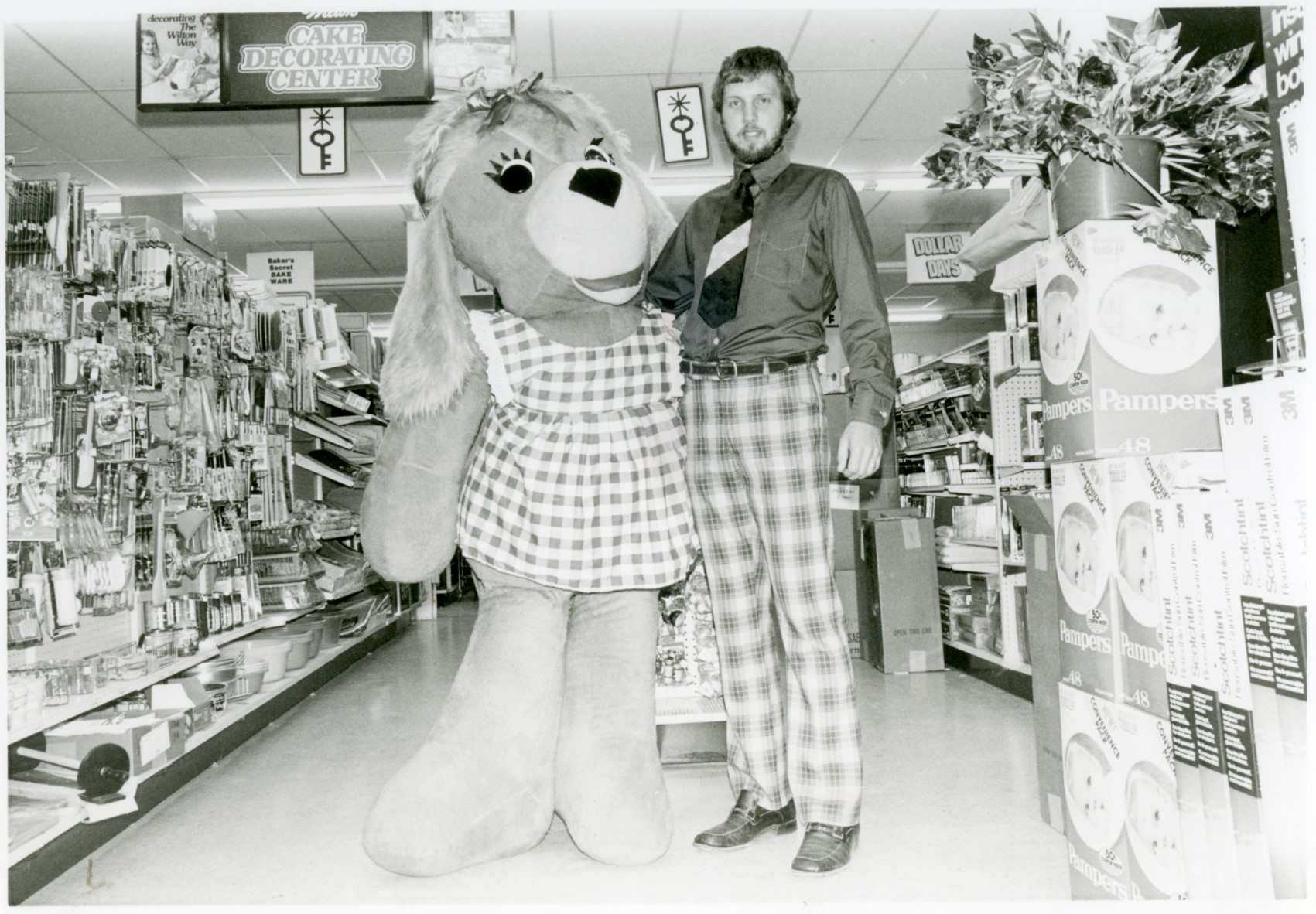 Black and white photo of Rob Stoll standing in his shop, Stoll’s Ben Franklin, with a person in a dog costume.