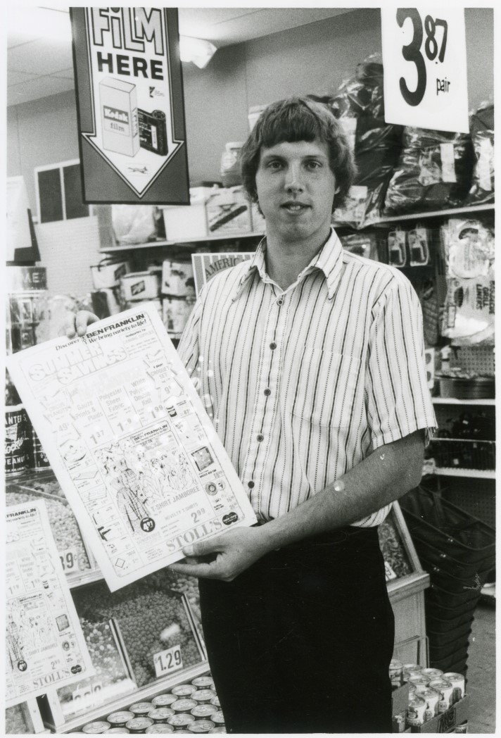 Black and white photo of Rob Stoll showing a map of his store, Stoll’s Ben Franklin.
