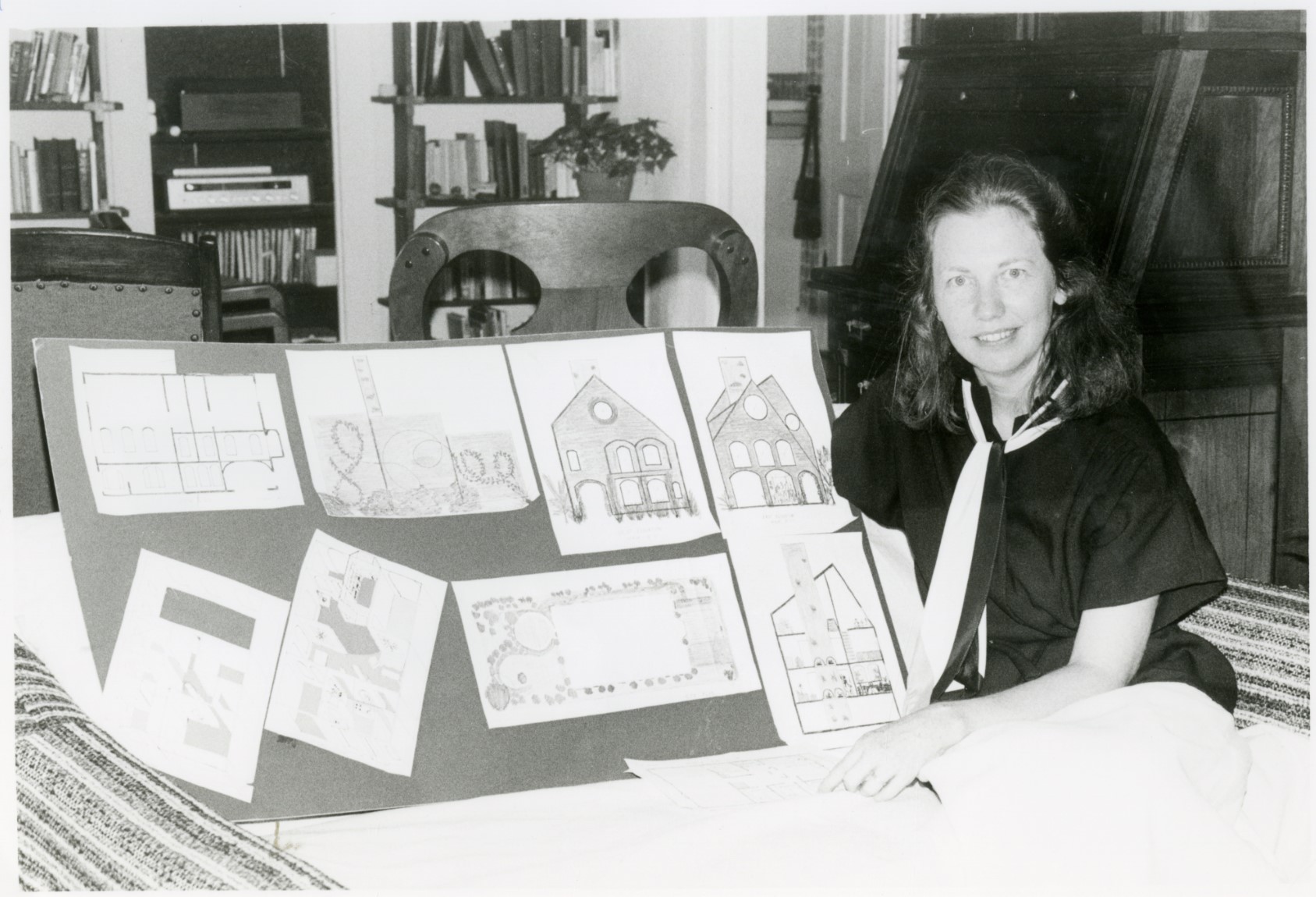 Black and white photo of Gretchen Sutherland standing beside her architectural drawings.