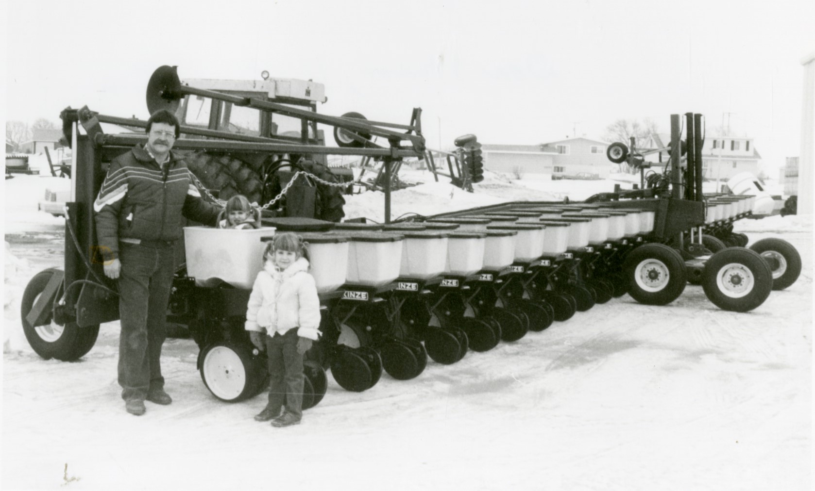 Black and white photo of Dan, Vicki, and Kim Stover standing beside (and in!) a tractor implement.