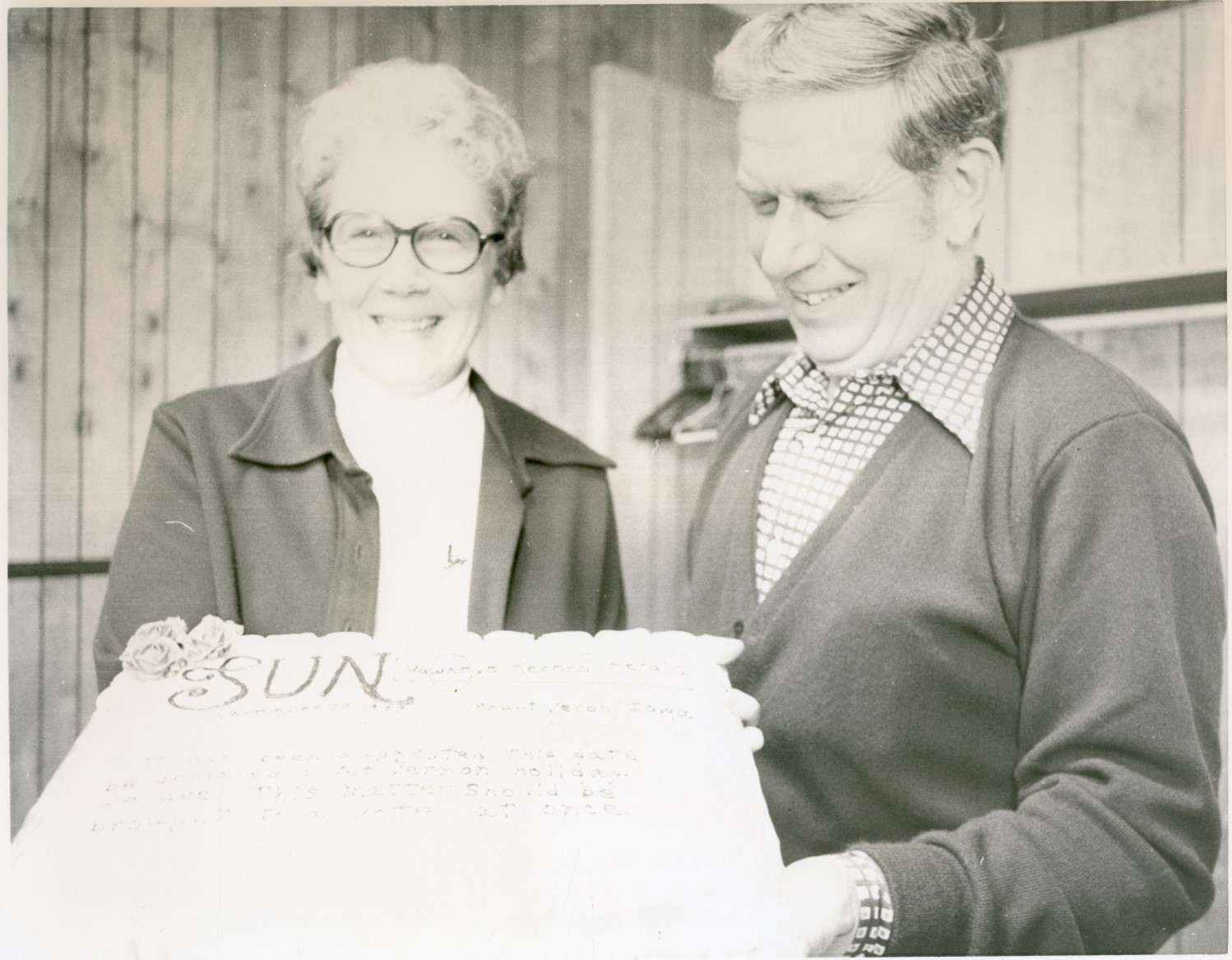 Black and white photo of Joann and Don Siggins holding a cake decorated like the Sun newspaper.