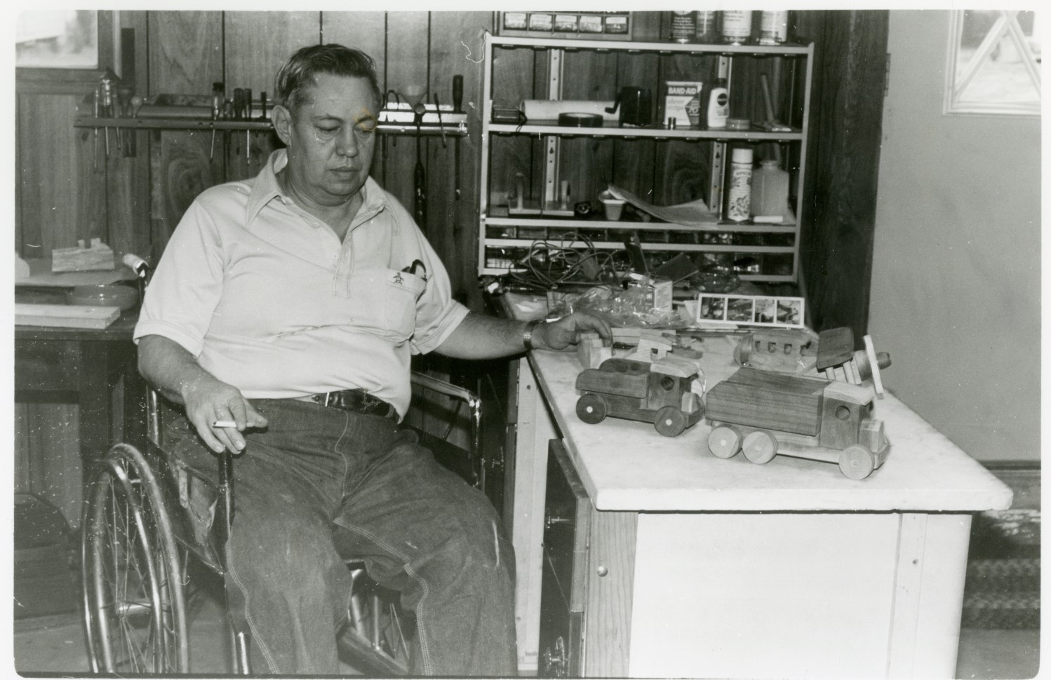 Black and white photo of Dale Travis looking at toy wooden trucks that he has made.